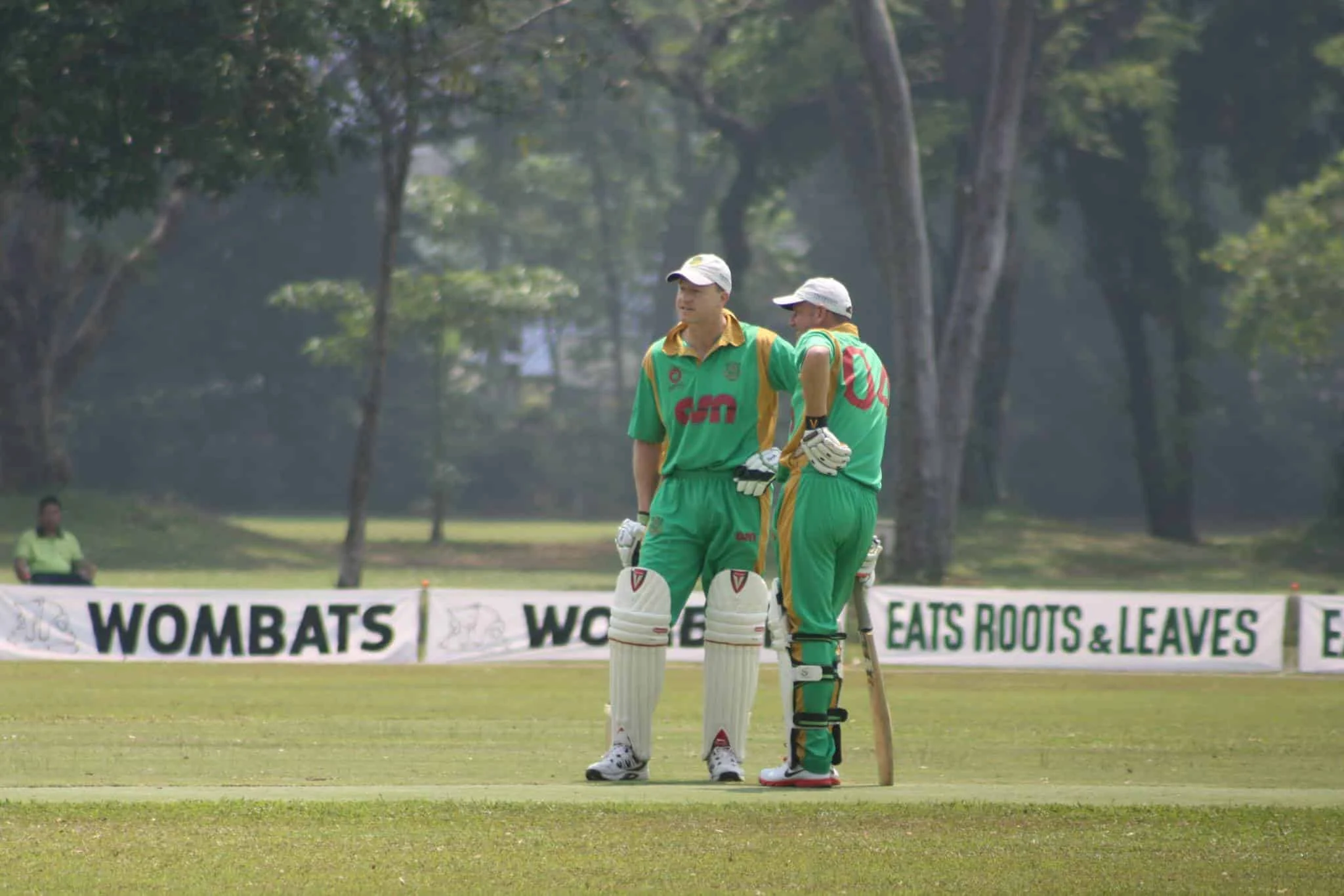 Two batsmen in green and gold kit at Chiang Mai Gymkhana Cricket Ground