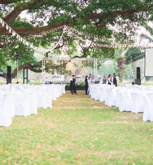 Outdoor wedding with white chairs and floral stage at Chiang Mai Gymkhana